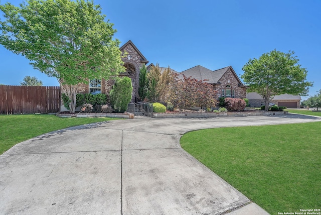 view of front of house with a front yard, brick siding, curved driveway, and fence