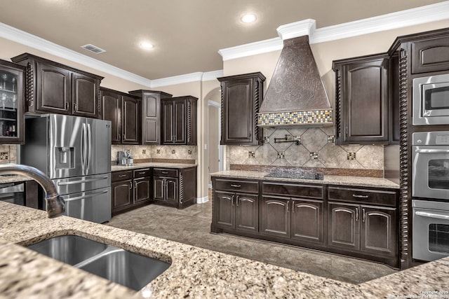 kitchen with stainless steel appliances, dark brown cabinets, a sink, visible vents, and premium range hood