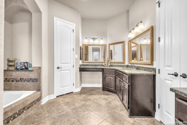 full bath featuring tiled bath, baseboards, and vanity
