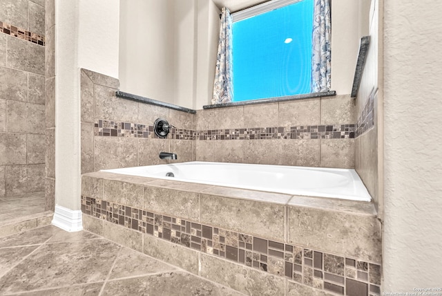 full bath with stone finish floor, a textured wall, and a bath