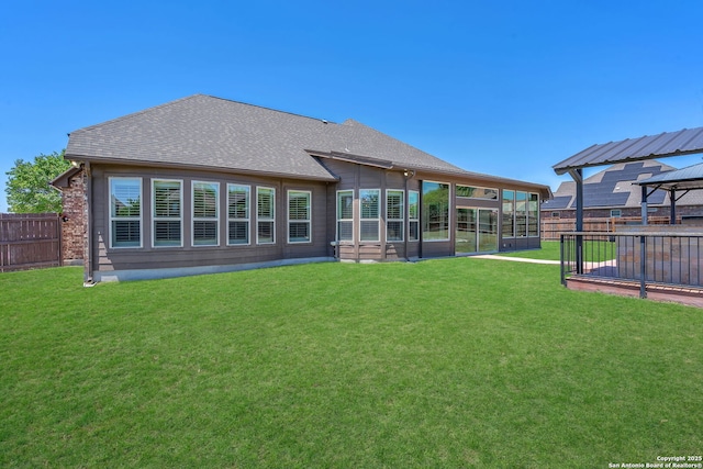 back of property featuring a sunroom, a yard, a shingled roof, and fence