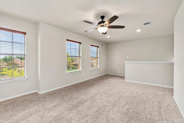 empty room with carpet flooring, a ceiling fan, baseboards, and visible vents