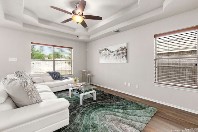 living room featuring ceiling fan, baseboards, wood finished floors, a tray ceiling, and visible vents