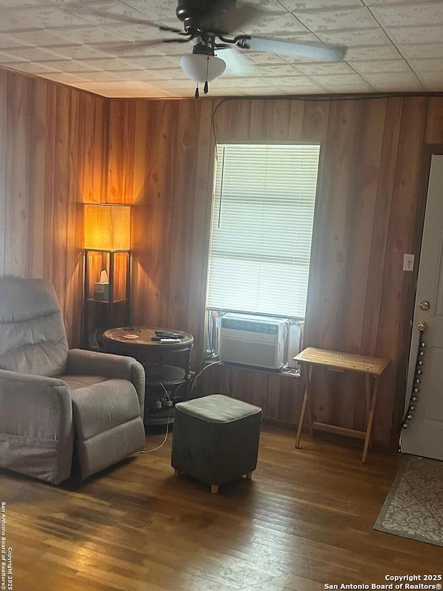 living area featuring hardwood / wood-style floors, ceiling fan, and wooden walls