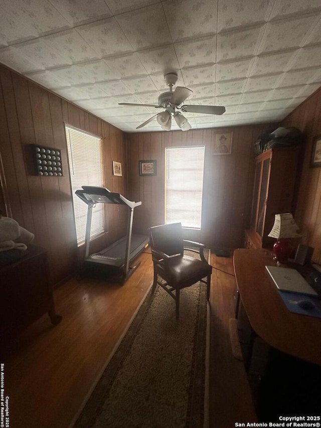 interior space featuring a healthy amount of sunlight, wood walls, wood finished floors, and ceiling fan