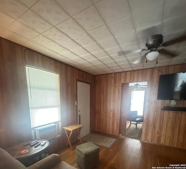 living area featuring wood walls, wood finished floors, and ceiling fan