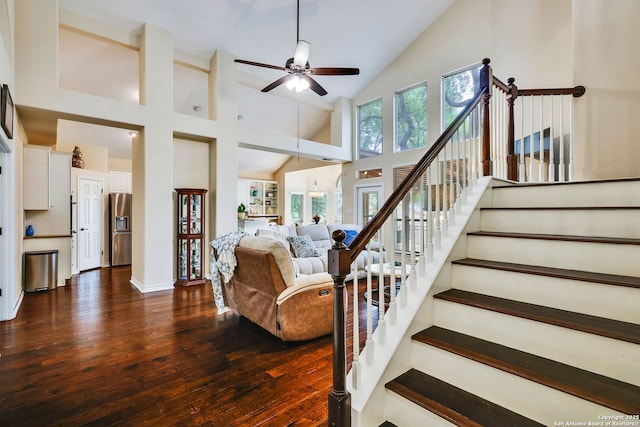 living area with high vaulted ceiling, ceiling fan, dark wood-style flooring, and stairs