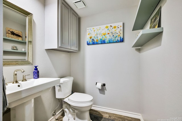 half bath featuring visible vents, wood finished floors, a sink, baseboards, and toilet