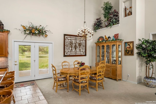 dining space with a towering ceiling, light colored carpet, a notable chandelier, and baseboards