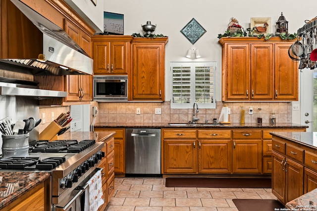 kitchen featuring appliances with stainless steel finishes, ventilation hood, brown cabinetry, and a sink
