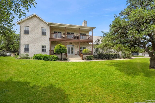 back of house featuring a yard, a balcony, french doors, and a chimney