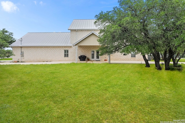 back of property featuring metal roof, a yard, and stone siding