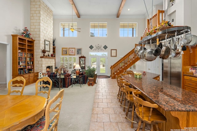dining area featuring stairs, a large fireplace, beam ceiling, a ceiling fan, and a high ceiling