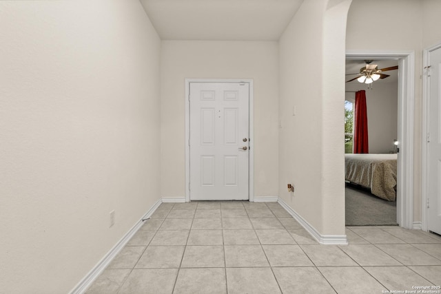 foyer with light tile patterned flooring, a ceiling fan, arched walkways, and baseboards