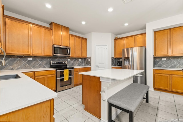 kitchen with brown cabinets, decorative backsplash, appliances with stainless steel finishes, a center island, and light tile patterned flooring