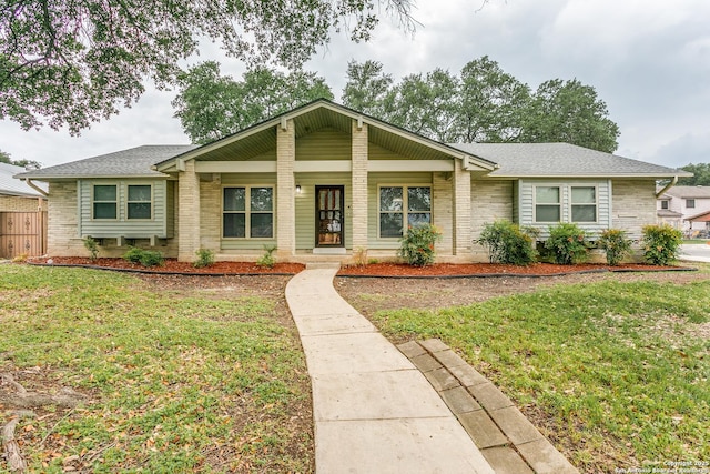 ranch-style home with a porch, roof with shingles, a front yard, and brick siding