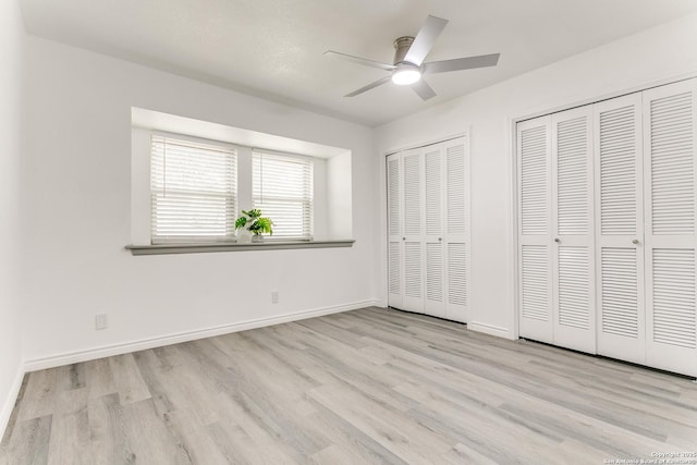 unfurnished bedroom featuring baseboards, wood finished floors, ceiling fan, and multiple closets