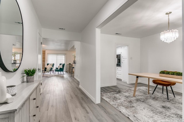 hallway with visible vents, baseboards, a chandelier, and light wood-type flooring