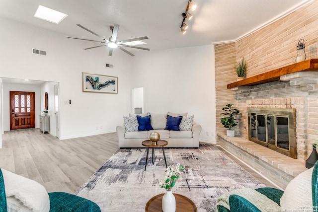 living room with a fireplace, a ceiling fan, visible vents, baseboards, and wood finished floors
