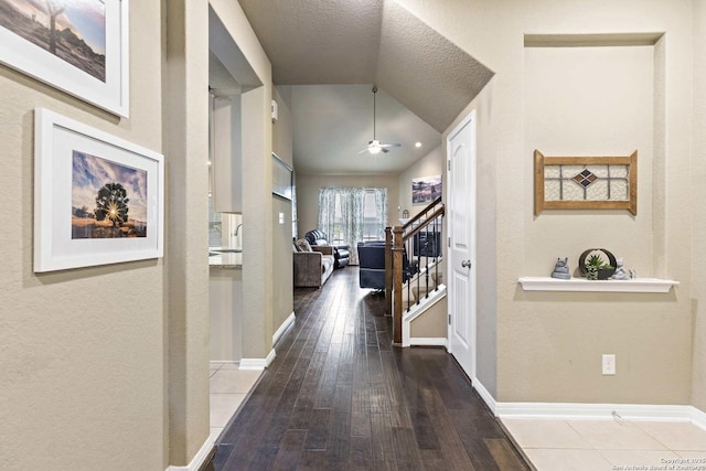 hallway with stairs, hardwood / wood-style floors, vaulted ceiling, baseboards, and a textured ceiling