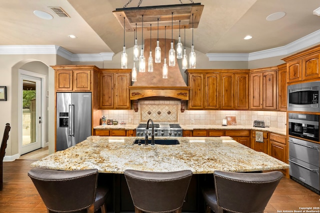 kitchen featuring lofted ceiling, a sink, stainless steel appliances, light stone countertops, and a center island with sink