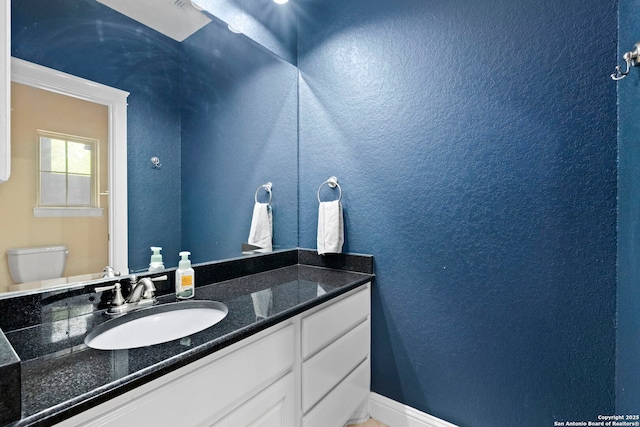 bathroom featuring toilet, a textured wall, vanity, and baseboards