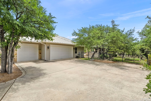 view of front facade with a standing seam roof, a garage, concrete driveway, stucco siding, and fence