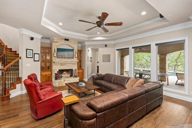 living area with a ceiling fan, hardwood / wood-style floors, stairway, and a raised ceiling