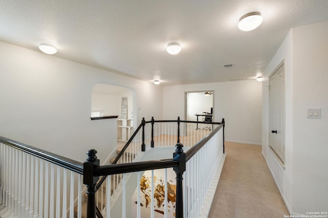hallway featuring an upstairs landing, visible vents, baseboards, arched walkways, and light carpet