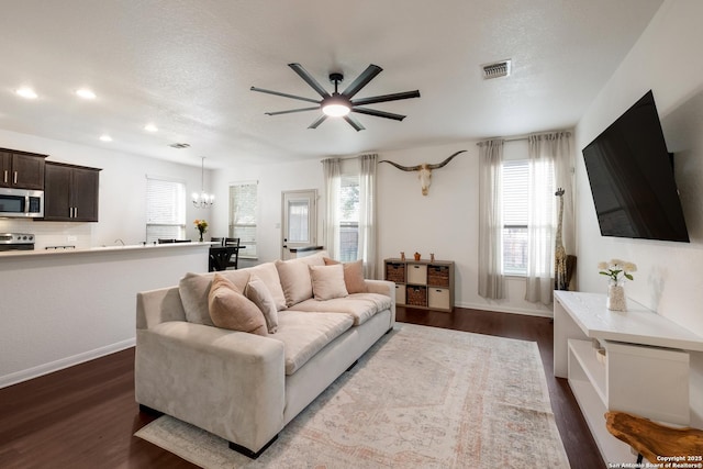 living room with recessed lighting, dark wood-type flooring, a healthy amount of sunlight, visible vents, and ceiling fan with notable chandelier