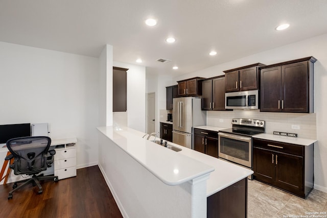 kitchen featuring stainless steel appliances, light countertops, dark brown cabinets, a sink, and a peninsula