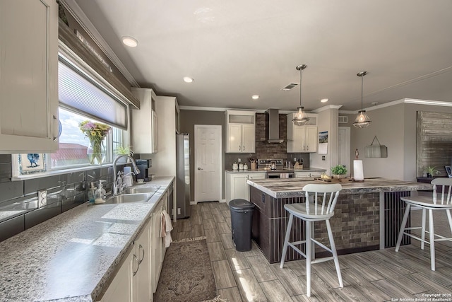 kitchen with wall chimney range hood, a breakfast bar area, decorative backsplash, a sink, and stainless steel appliances