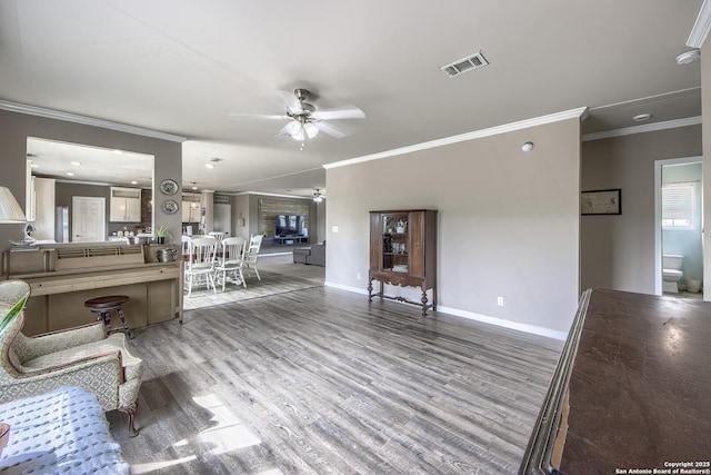 living area with baseboards, visible vents, ornamental molding, and ceiling fan
