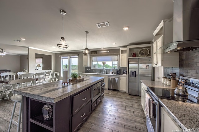kitchen featuring open shelves, tasteful backsplash, a breakfast bar, wall chimney range hood, and appliances with stainless steel finishes