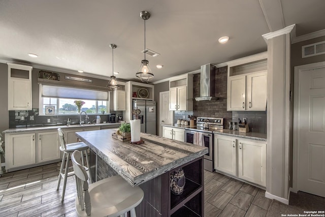 kitchen featuring tasteful backsplash, appliances with stainless steel finishes, ornamental molding, a sink, and wall chimney exhaust hood