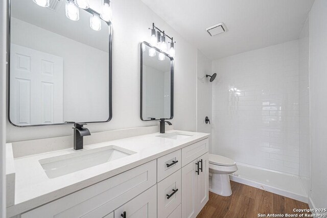 full bathroom with wood finished floors, toilet, tiled shower, and a sink