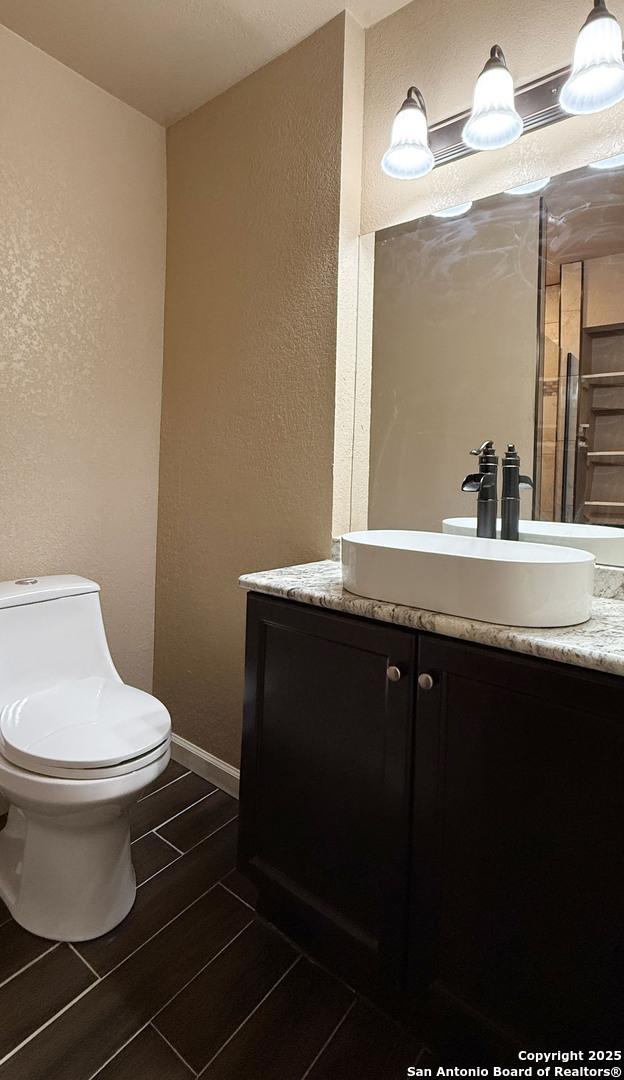 7274 Fm 327, Elmendorf, TX 78112 - bathroom with toilet, a textured wall, vanity, baseboards, and wood finish floors