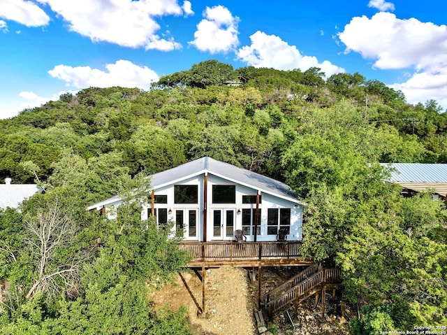 rear view of house with a deck, metal roof, french doors, and a forest view