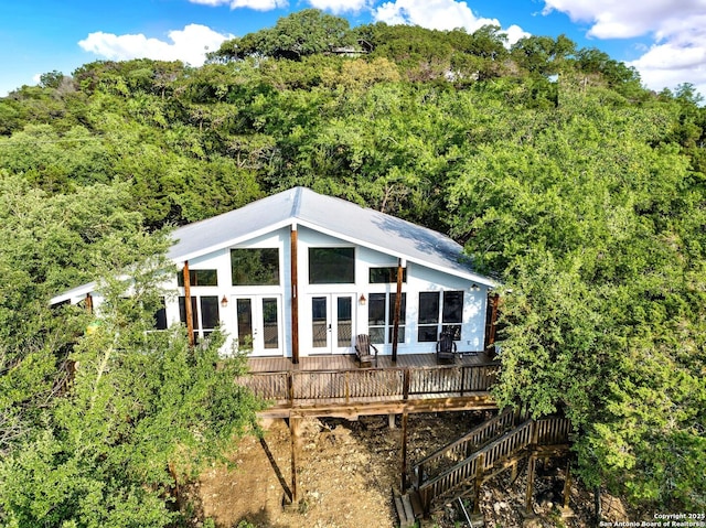 back of property featuring a wooded view, french doors, and a wooden deck