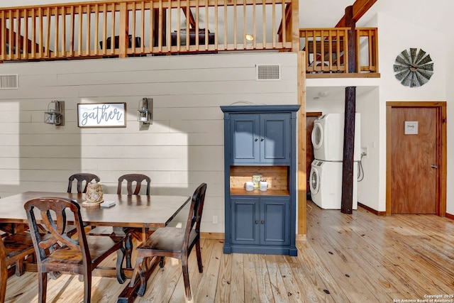 dining space with light wood-style flooring, visible vents, stacked washer / drying machine, baseboards, and wooden walls