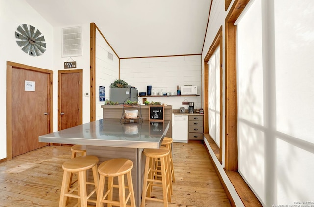 kitchen with lofted ceiling, a breakfast bar area, stainless steel counters, light wood finished floors, and white appliances