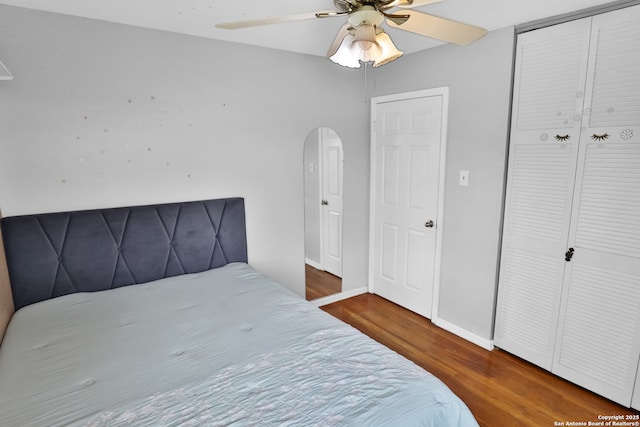 bedroom featuring ceiling fan, a closet, baseboards, arched walkways, and wood finished floors