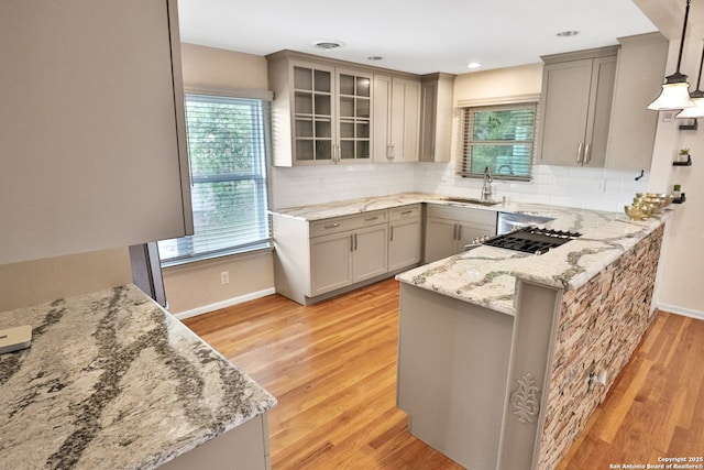 kitchen featuring light stone counters, a healthy amount of sunlight, a peninsula, and a sink
