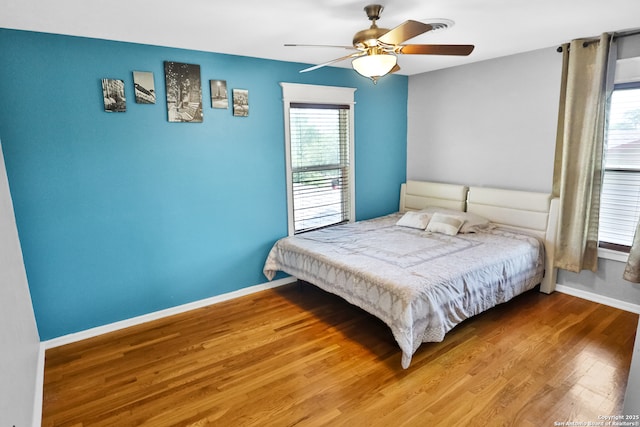 bedroom with baseboards, wood finished floors, a ceiling fan, and multiple windows