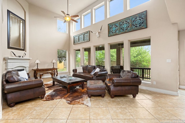 tiled living room featuring a fireplace, a towering ceiling, ceiling fan, and baseboards