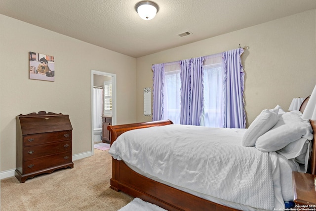 bedroom featuring ensuite bath, visible vents, baseboards, a textured ceiling, and light colored carpet