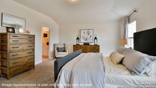 bedroom with carpet floors, ensuite bathroom, and vaulted ceiling