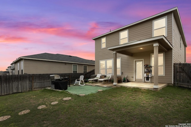 back of property at dusk featuring a lawn, a fenced backyard, and a patio area