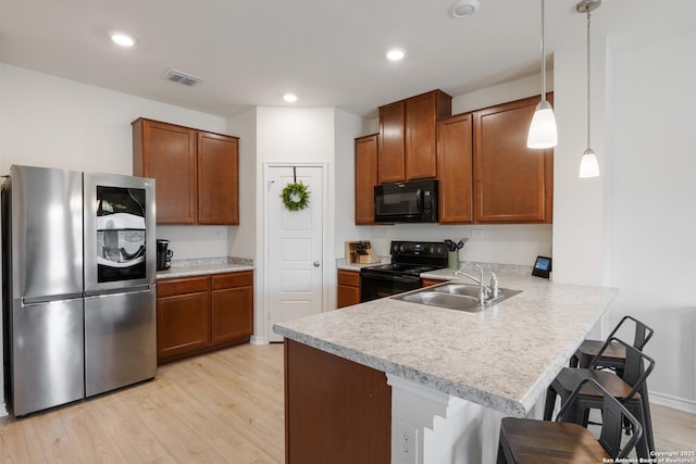 kitchen featuring light wood-style flooring, a breakfast bar area, light countertops, black appliances, and a sink
