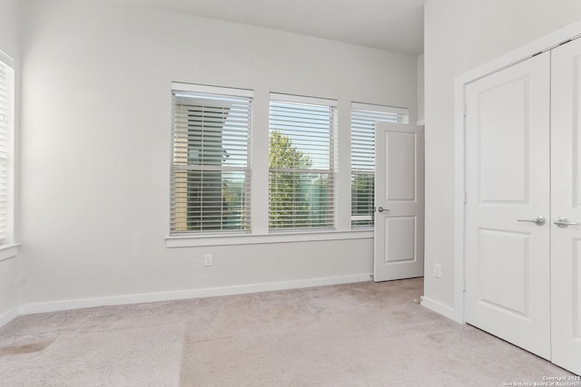 unfurnished bedroom with a closet, light carpet, and baseboards